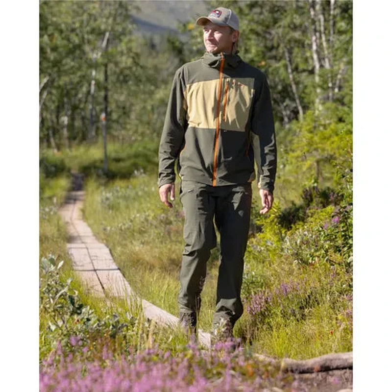 Man i mörkgröna vandringsbyxor vandrar på träbro i natur