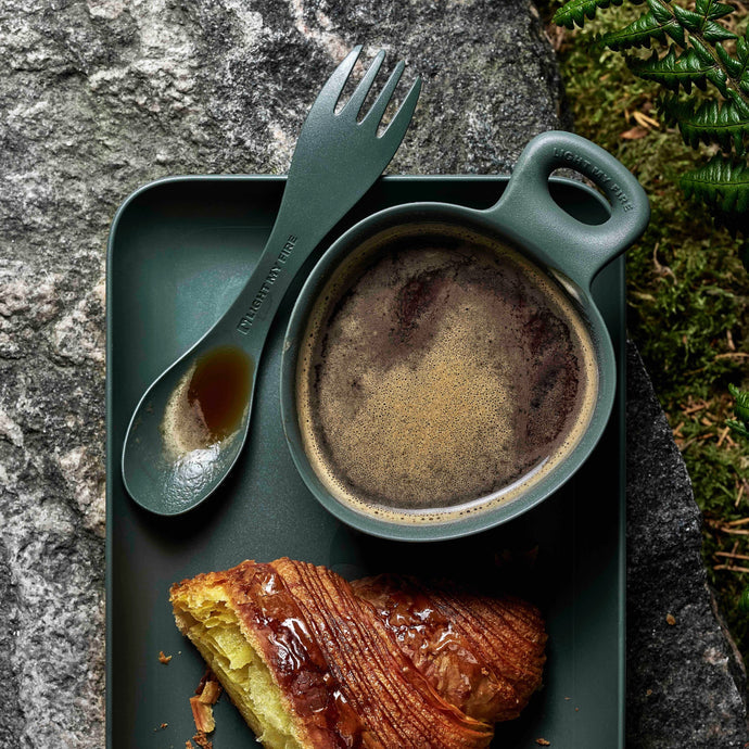 Mörkgrön kåsa med kaffe och spork på grön bricka