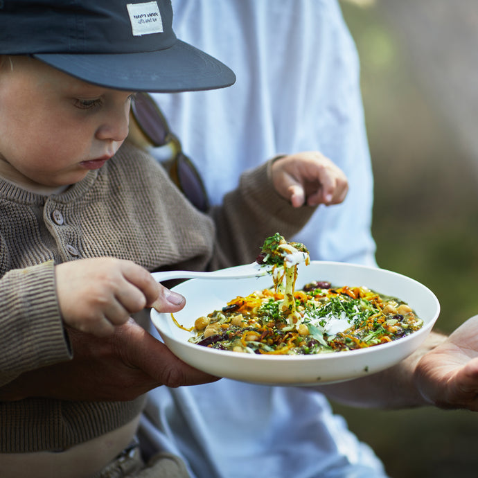 Barn äter med vit spork från skål utomhus