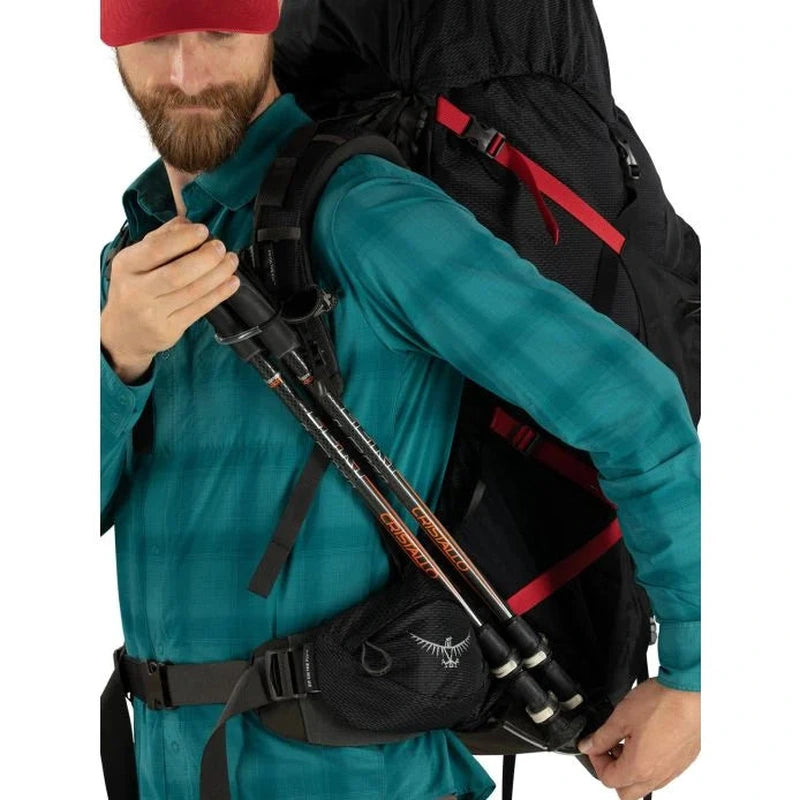 Osprey Aether Plus 85 herrryggsäck i svart med röda remmar, buren av man med vandringspinnar