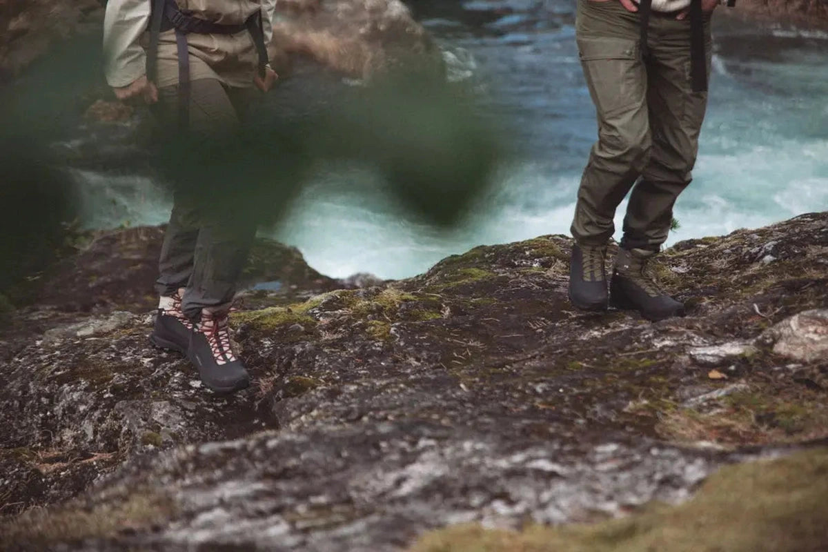 Lågvinkelbild av ben i svarta och gråa Alfa Gneis GTX kängor vid vattendrag