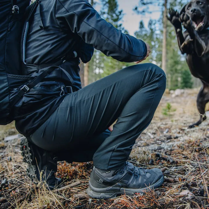 Man knekar sig i skog med svarta Salomon vandringskängor