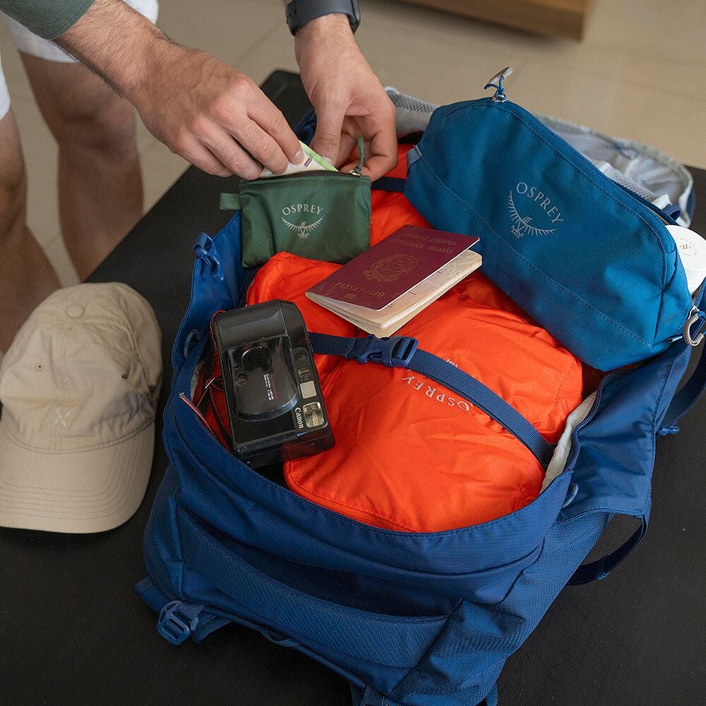 Osprey Farpoint 55 öppen packad med kamera, pass och inpackningspåsar för resa